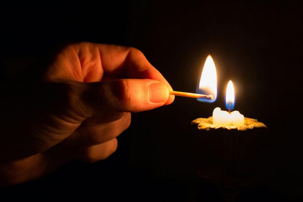 A hand uses a match to light a candle in a dimly lit environment.