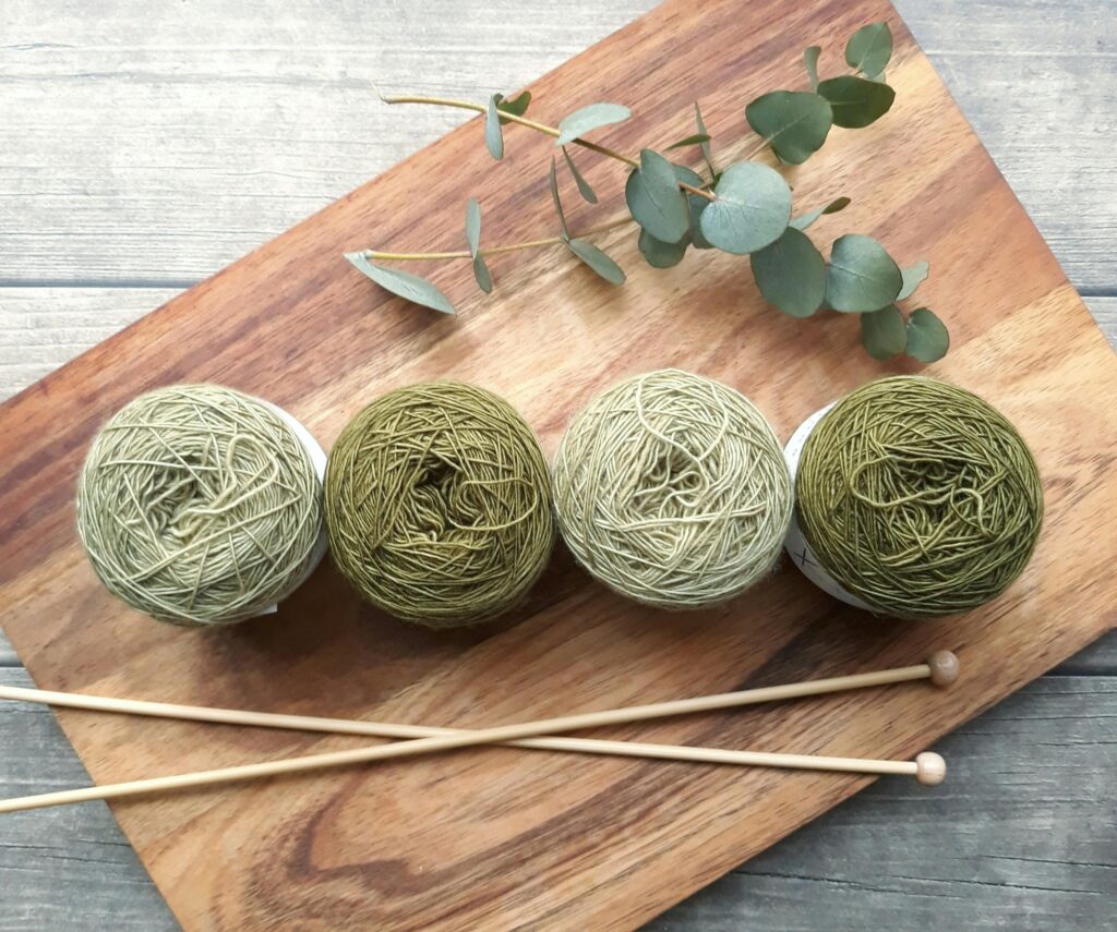 A flat lay of green yarn balls and knitting needles on wood, evoking creativity and craftsmanship.